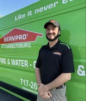 A man with a black polo in front of  a green van. 