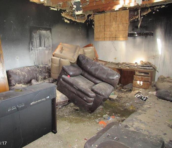 A living room with black couches and a patch in the wall from a fire