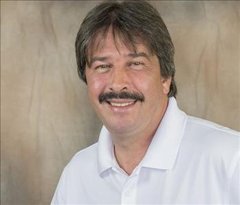 A male with dark brown hair and a mustache wearing a white shirt.